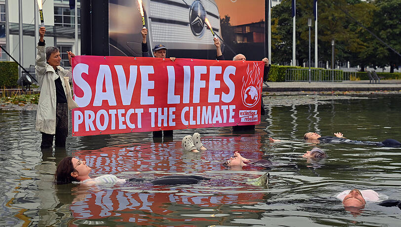 IAA-Proteste von Extinction Rebellion auf dem Messegelände: Die Aktivisten hissen ein Banner und treiben "tot" im Wasser des Sees vor dem Haupteingang. IAA-Proteste von Extinction Rebellion auf dem Messegelände: Die Aktivisten hissen ein Banner und treiben "tot" im Wasser des Sees vor dem Haupteingang.
