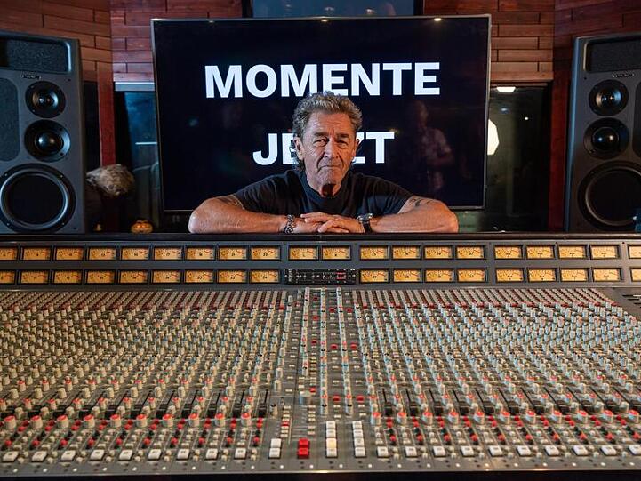 Peter Maffay lächelt, hinter dem Mischpult stehend und vor einer Wand, auf der "Momente Jetzt" zu sehen ist. Foto: Peter Kneffel/Archiv