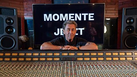 Peter Maffay lächelt, hinter dem Mischpult stehend und vor einer Wand, auf der "Momente Jetzt" zu sehen ist. Foto: Peter Kneffel/Archiv