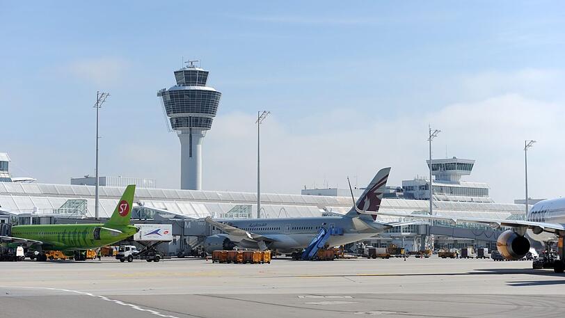 Mehrere Flugzeuge stehen auf dem Flughafen München an einem Terminal vor dem Tower.