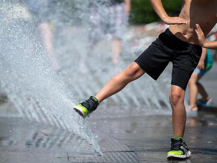 Ein Junge spielt am Stachus in München mit dem Wasser von einem Brunnen.