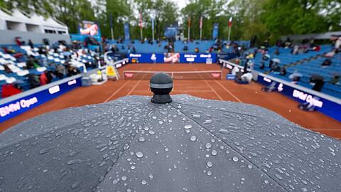 Zuschauer sitzen mit Regenschirmen auf der Tribüne.