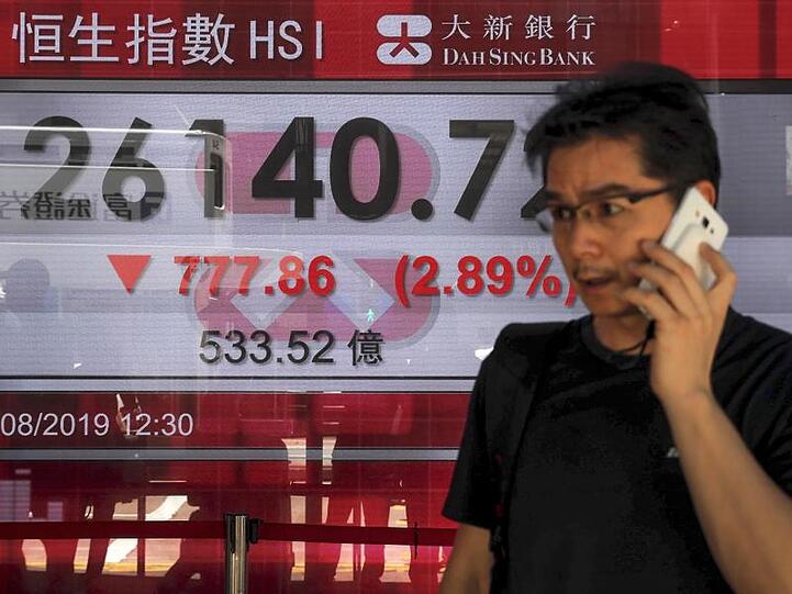 Ein Mann telefoniert in Hongkong vor einer Anzeigetafel mit dem Hong Kong Composite Index.