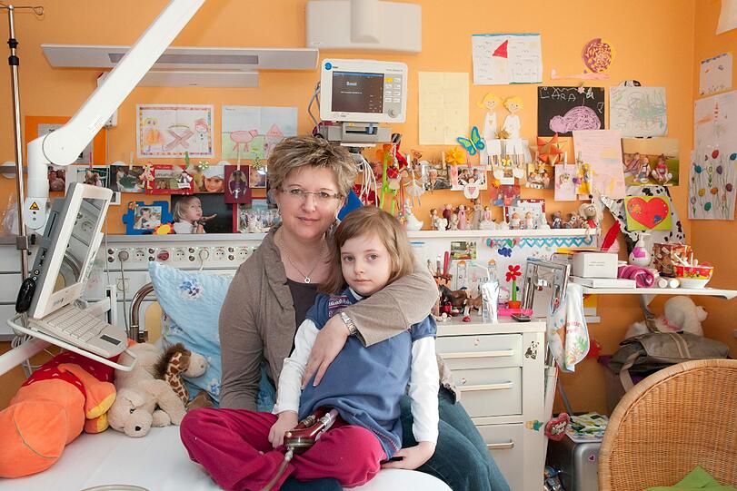 Die kleine Lara sitzt mit ihrer Mutter im Krankenzimmer des Klinikums Erlangen. Auf ihrem Schoß: die Schläuche, die ihre Brust mit dem Kunstherz verbinden.