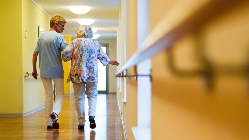 Eine Pflegekraft geht in einem Pflegeheim mit einer älteren Dame über einen Korridor. Foto: Christoph Schmidt/Archivbild