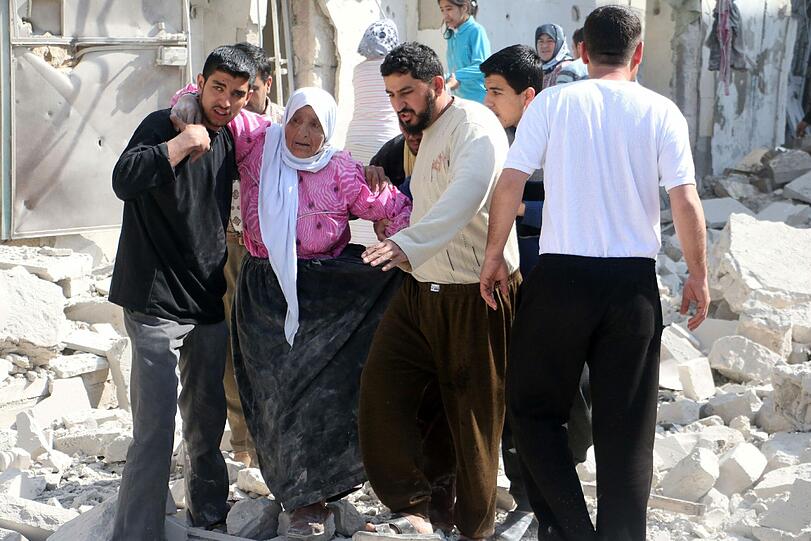 Mehrere Männer stützen eine syrischen Frau auf ihrem Weg durch die Trümmerberge nach einem Luftangriff der syrischen Regierung auf die Stadt Aleppo.