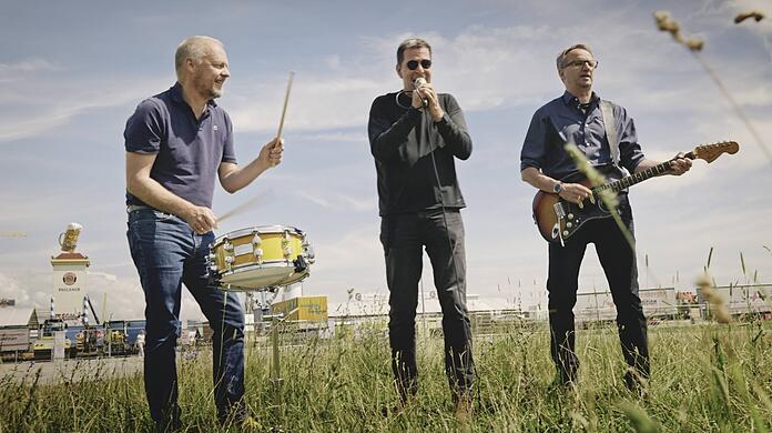 Musikvideo-Dreh auf der Theresienwiese: Hier spielen Philipp Meyer, Christian CT Türck und Ralf Bremer (v.l.) ihren bayerischen Rocksong "Oktoberfest" - im Hintergrund wird gerade die aktuelle Wiesn aufgebaut.