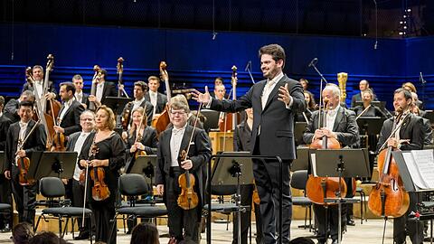 Mit einladender Geste: Lahav Shani mit Musikerinnen und Musikern des Israel Philharmonic Orchestra und der Münchener Philharmoniker in der Isarphilharmonie.