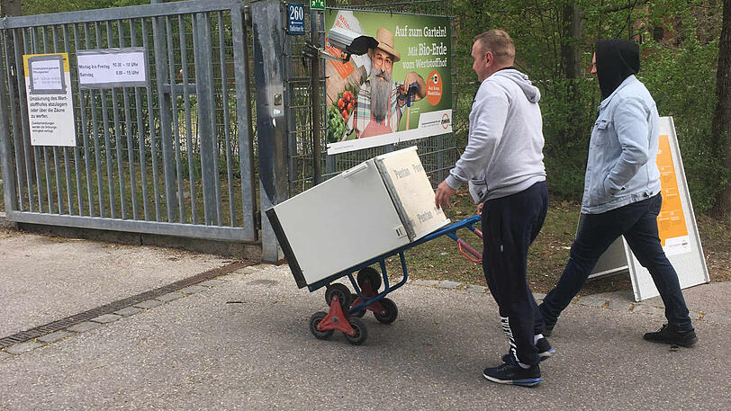 Zwei Männer fahren einen alten Kühlschrank zum Wertstoffhof.
