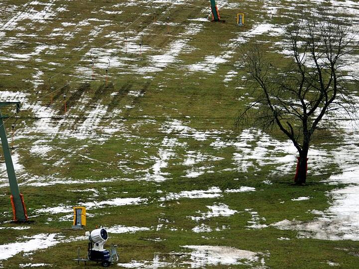 Ein Schneekanone steht in einem grün-weißen Fleckenteppich an einer Skipiste. Foto: Patrick Seeger/dpa