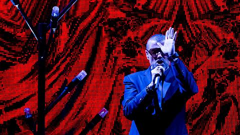 George Michael sang mit großem Orchester vor einem riesigen roten Vorhang.