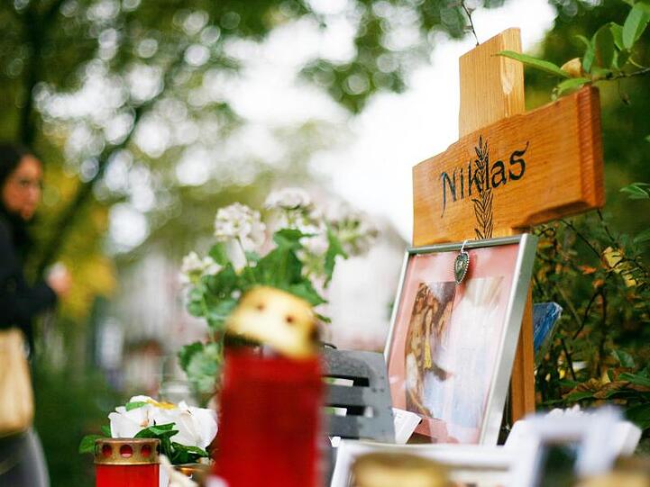Blumen und Kerzen stehen in Bonn neben einem Holzkreuz an der Stelle, an der der später verstorbene Niklas P. von Schlägern attackiert wurde.