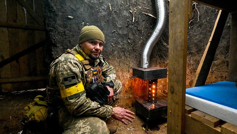 Ein ukrainischer Soldat wärmt sich an einem Ofen.