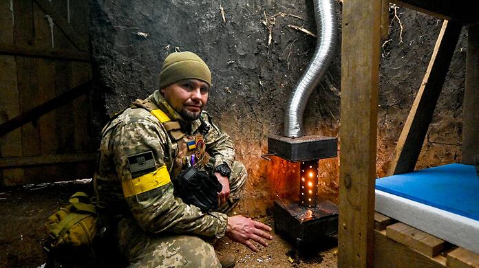 Ein ukrainischer Soldat wärmt sich an einem Ofen.