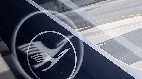 Ein Flugzeug mit dem Logo der Lufthansa auf der Heckflosse steht an einem Flughafen.