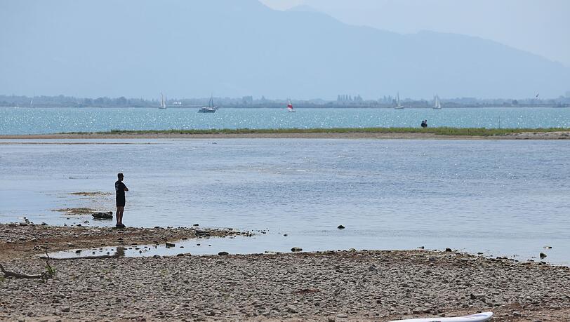 Es bleibt heiß in Bayern: Ein Mann steht am trockenen Ufer des Bodensees neben einem Surfboard. (Archivbild) Es bleibt heiß in Bayern: Ein Mann steht am trockenen Ufer des Bodensees neben einem Surfboard. (Archivbild)