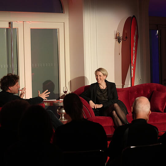 Adrian Prechtel im Gespräch mit Bürgermeisterin Katrin Habenschaden auf dem roten Sofa (von Möbel Höffner) in München.