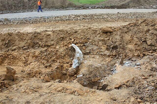 Ein Bauarbeiter läuft an einer Baustelle vorbei, an der ein verbogener Propeller aus dem Erdreich ragt.