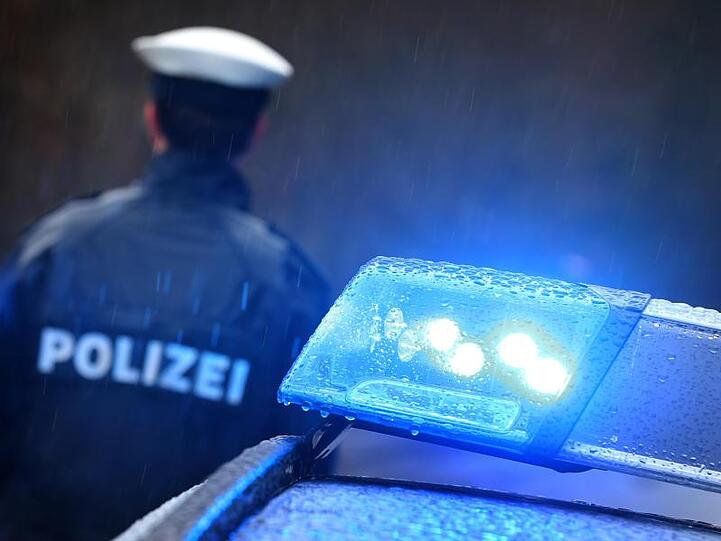 Ein Polizist steht im Regen vor einem Streifenwagen dessen Blaulicht aktiviert ist. Foto: Karl-Josef Hildenbrand/dpa