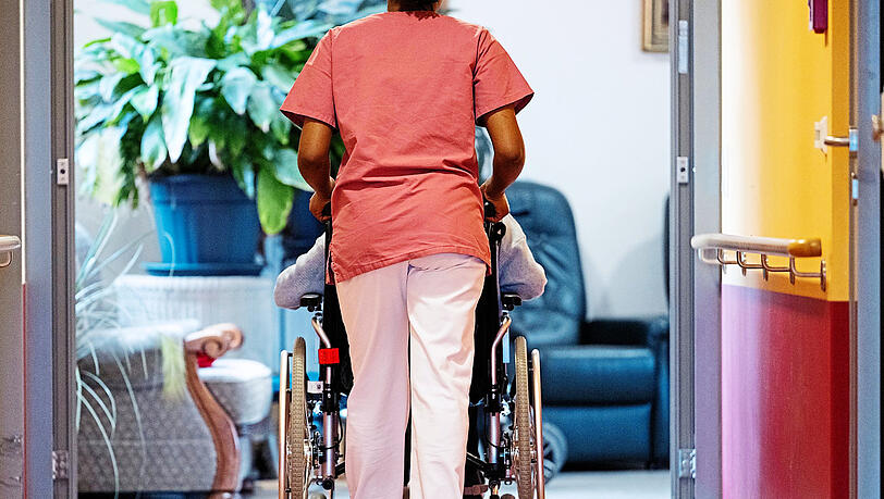 Eine Pflegerin schiebt eine Seniorin in einem Heim den Gang entlang. Nicht nur der Eigenanteil für Pflegebedürftige steigt immer weiter, auch die Pflegekassen geraten finanziell immer stärker in Bedrängnis.