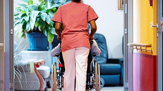 Eine Pflegerin schiebt eine Seniorin in einem Heim den Gang entlang. Nicht nur der Eigenanteil für Pflegebedürftige steigt immer weiter, auch die Pflegekassen geraten finanziell immer stärker in Bedrängnis.