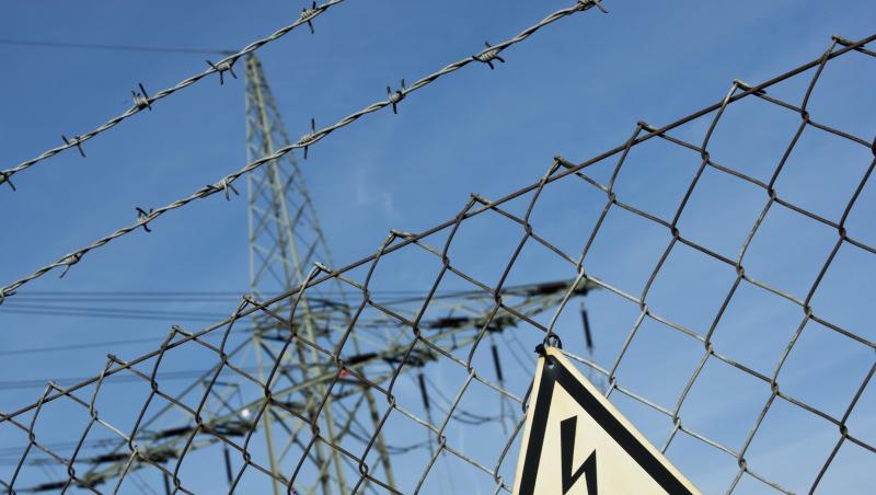 Ein Gefahrenschild für Elektrizität ist vor einer Stromtrasse zu sehen. Foto: Daniel Naupold/Archiv