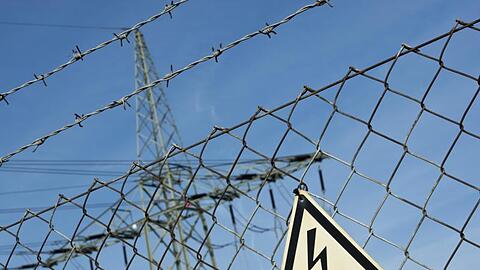 Ein Gefahrenschild für Elektrizität ist vor einer Stromtrasse zu sehen. Foto: Daniel Naupold/Archiv