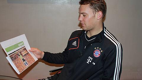 Manuel Neuer blickt auf eine Fotomontage der Abendzeitung, die ihn im Tor des FC Bayern vor einer Mauer zeigt.