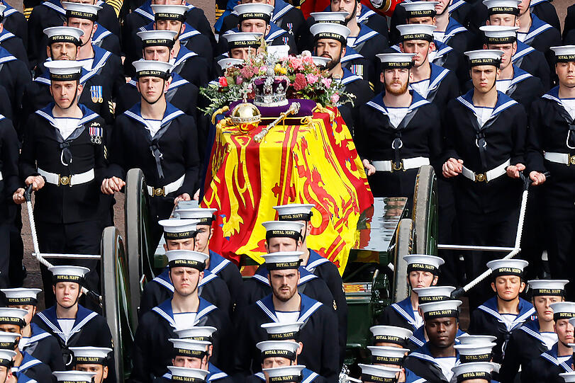 Der Sarg von Königin Elizabeth II. mit der königlichen Standarte, der Imperial State Crown, dem Reichsapfel und Zepter wird in einer feierlichen Prozession auf einer Lafette die Straße The Mall entlang gezogen.