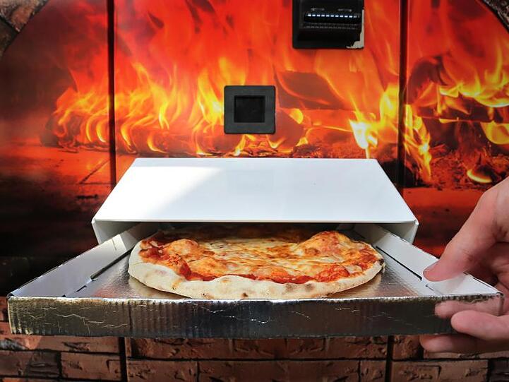 Ein Kunde greift nach einer Pizza Margherita die nach etwa drei Minuten Backzeit aus einem Automaten ausgeworfen wird. Foto: Karl-Josef Hildenbrand/dpa