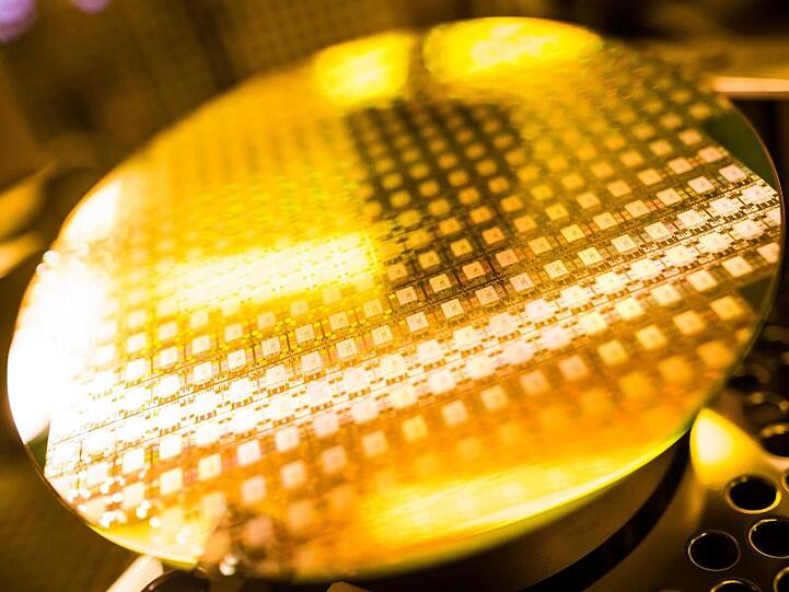 Ein Wafer (Halbleiterscheibe) glänzt im Licht einer Lampe. Foto: Christoph Schmidt/Archivbild