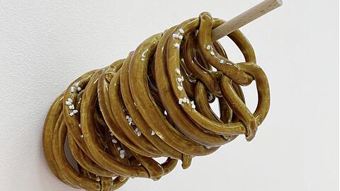 Wer Marjan Baniasadis Installation „Brezeln mit oder ohne“ von 2024 erwirbt, muss zumindest optisch nie mehr hungern und landet - Keramik macht‘s möglich - auch nicht in der Carb- oder Kohlehydrat-Falle.