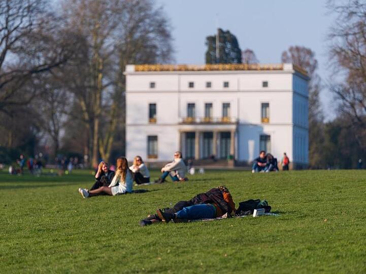 Menschen genießen das sonnige Wetter auf einer Wiese vor dem Jenisch-Haus in Hamburg.