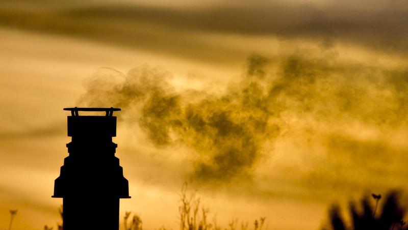Ein kleiner Schornstein auf einem bepflanzten Dach entlässt bei Sonnenaufgang die Abgase einer Gasheizung in die eiskalte Morgenluft.