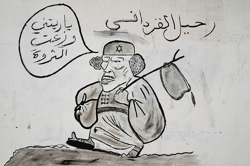 Diese Karikatur zeigt einen reumütigen Gaddafi, der mit Sack und Pack sein Land verlässt. Seine Sprechblase liest: "Ich hätte meinen Reichtum mit dem Volk teilen sollen." Die Rebellen nutzen die neuen Freiheiten seit Beginn der Ausschreitungen und machen sich in der Öffentlichkeit künstlerisch über Gaddafi lustig.