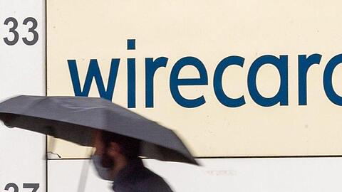 Ein Mann mit Regenschirm geht vor dem Schriftzug von Wirecard.