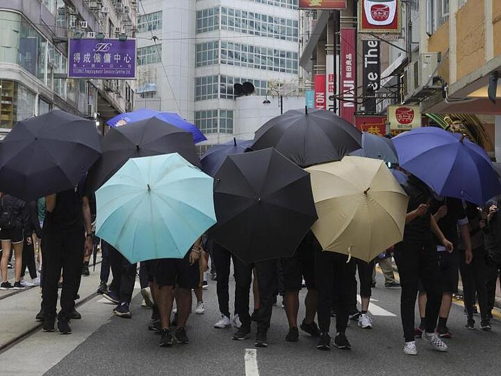 Demonstranten bilden ein Schutzschild aus Regenschirmen.