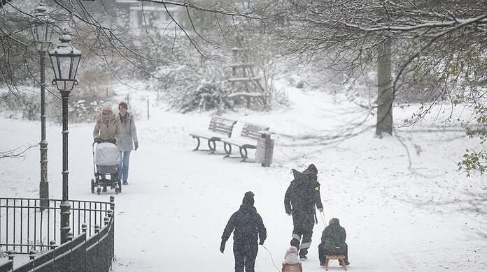 Menschen spazieren durch den verschneiten Volkspark Friedrichshain in Berlin.