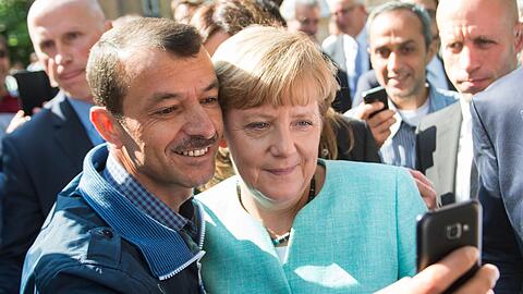 Bald zehn Jahre her: Angela Merkel (CDU) lässt sich nach dem Besuch einer Erstaufnahmeeinrichtung für Asylbewerber in Berlin-Spandau für ein Selfie zusammen mit einem Flüchtling fotografieren. (Archivbild)
