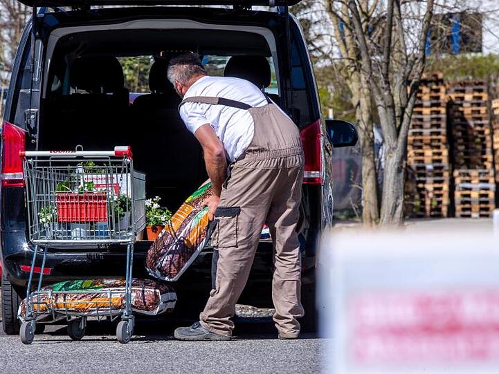 Ein Mann hebt Säcke mit Rindenmulch von einem vollen Einkaufswagen vor einem wieder eröffneten Bau- und Gartenmarkt in sein Auto. Foto: Jens Büttner/dpa-Zentralbild/dpa/Archivbild
