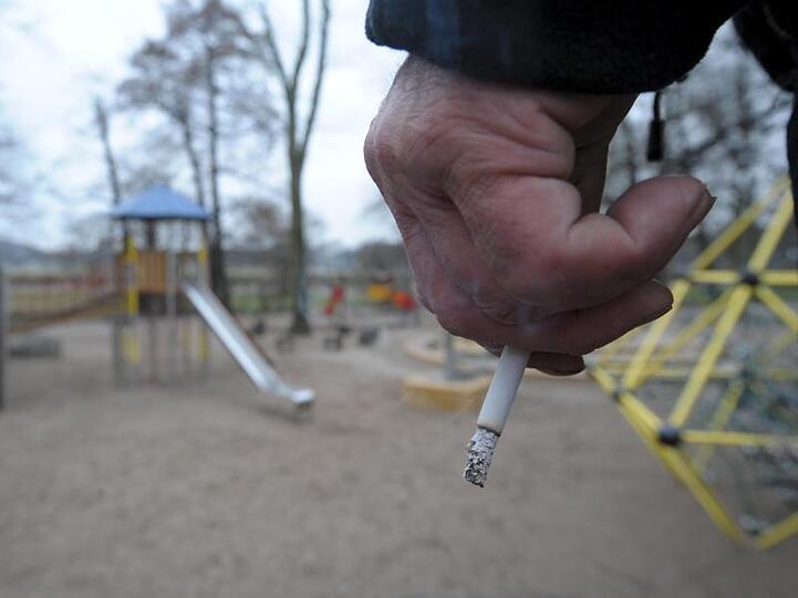 Ein Mann hält auf einem Spielplatz eine Zigarette in der Hand.