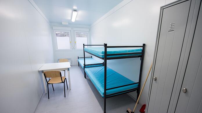 Blick in ein Zimmer mit drei Betten in einem Wohncontainer in einer Erstaufnahmeunterkunft.