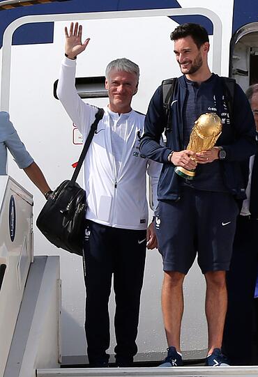 Hugo Lloris (M), Torhüter der französischen Fußballnationalmannschaft, hält den Siegerpokal am Flughafen Charles de Gaulle in Paris.