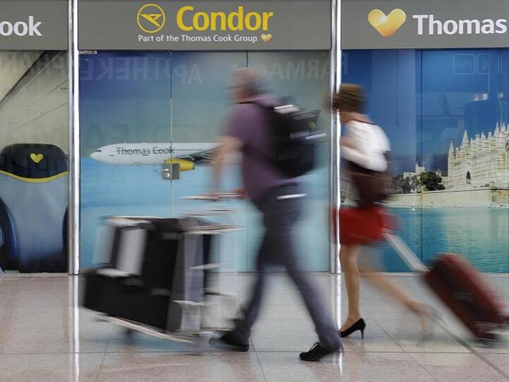 Passagiere gehen an einem Büro von Condor und Thomas Cook am Flughafen Palma de Mallorca vorbei.