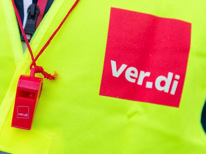 Ein Streikender trägt eine Warnweste mit dem Verdi-Logo und eine rote Trillerpfeife. Foto: Christophe Gateau/Archiv