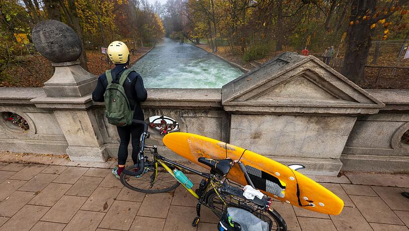 Ein Mann mit einem Surfboard an seinem Fahrrad schaut von einer Br&uuml;cke auf die - nicht mehr vorhandene - Eisbachwelle im Englischen Garten.