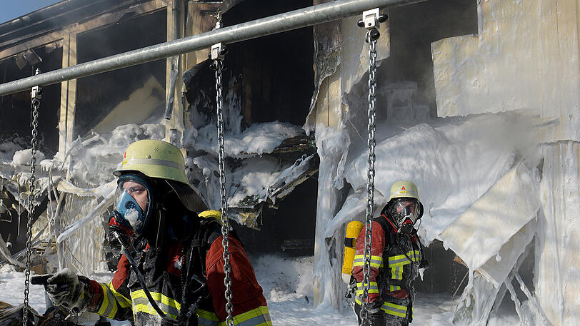 Feuerwehrleute stehen vor ausgebrannten Wohncontainern. Nachts kam es in dieser Asylunterkunft aus unbekannter Ursache zu einem Brand, bei dem drei Bewohner verletzt wurden.