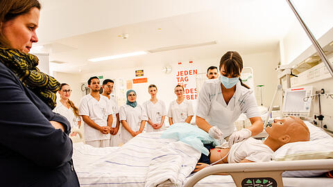 Die dritte Bürgermeisterin Verena Dietl (SPD) schaut einer Pflegekraft im neuen Kompetenzzentrum Internationale Pflege (KIP) der München Klinik bei der Betreuung einer Patienten-Puppe zu.