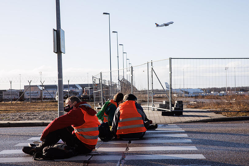 Aktivisten der Gruppe "Die letzte Generation" haben sich mit ihren Händen auf einen Zebrastreifen auf der Südallee, einer Zufahrt zum Frachtbereich vom Münchner Flughafen, geklebt.