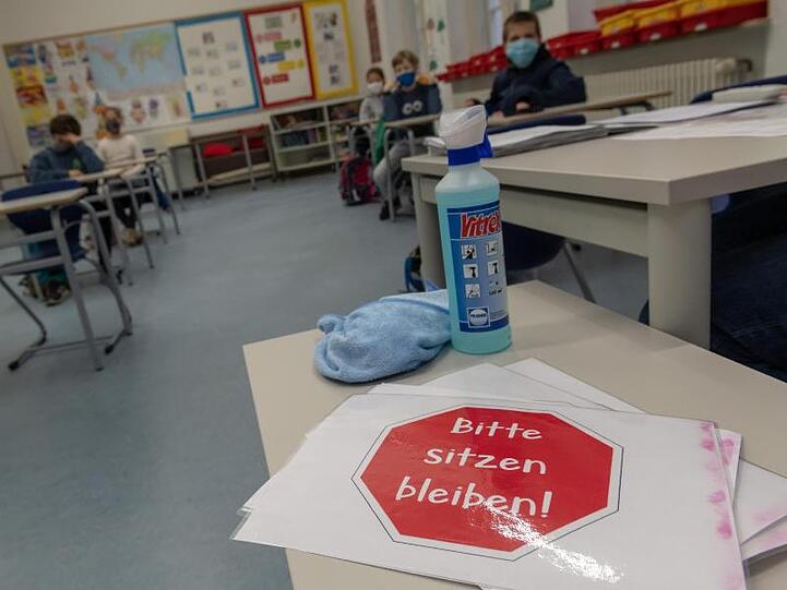 Ein Schild mit der Aufschrift "Bitte sitzen bleiben!" liegt auf einem Tisch im Klassenraum einer vierten Klasse. Foto: Peter Kneffel/dpa